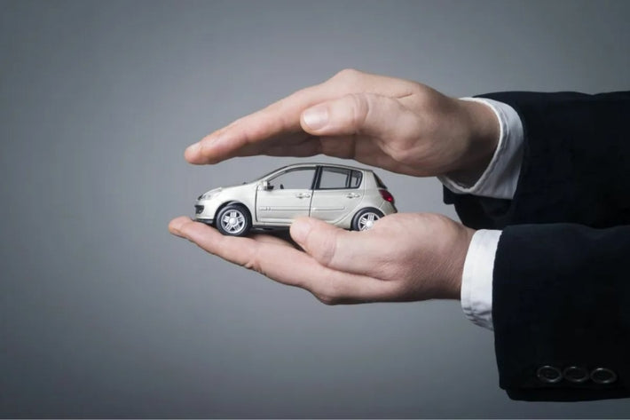 Mains de professionnel entourant une miniature de voiture grise pour l assurance auto