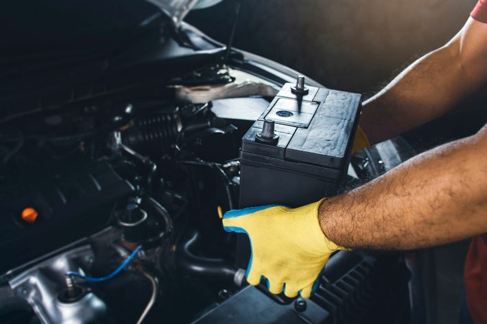 Un mécanicien portant des gants jaunes remplace la batterie de voiture sous le capot
