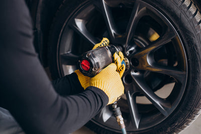 Mécanicien avec gants jaunes serrant les écrous d une jante de voiture à la clé à choc