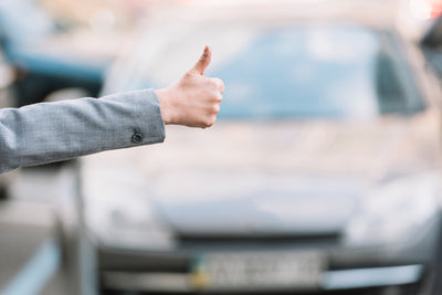 Une personne tend le pouce devant une voiture floue pour illustrer l assurance auto avec malus