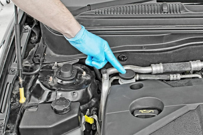 Un mecanicien avec gant bleu designe l emplacement du liquide d embrayage sous le capot