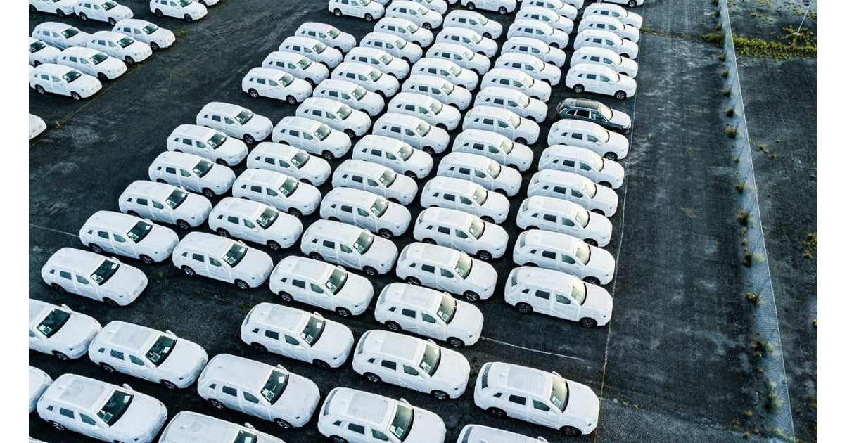 Vue aerienne de nombreux vehicules neufs blancs alignes sur un parc de stockage de flotte automobile