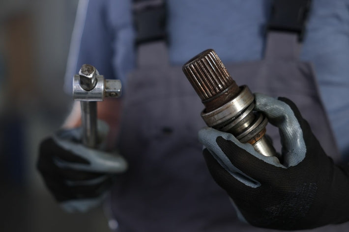 Mécanicien avec gants de protection présentant un arbre de transmission après équilibrage
