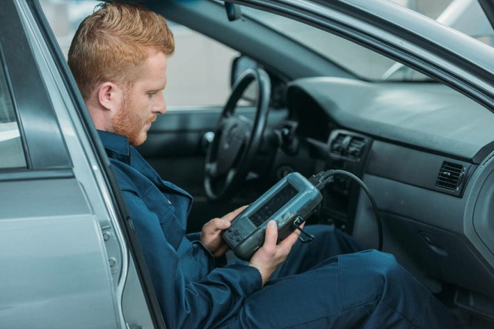 Mécanicien assis dans une voiture utilisant une valise de diagnostic multimarque iCarsoft