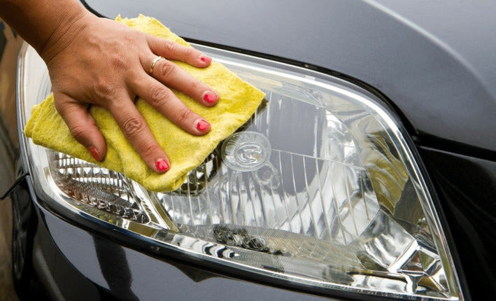 Nettoyage manuel du phare avant d'une voiture noire avec un chiffon jaune