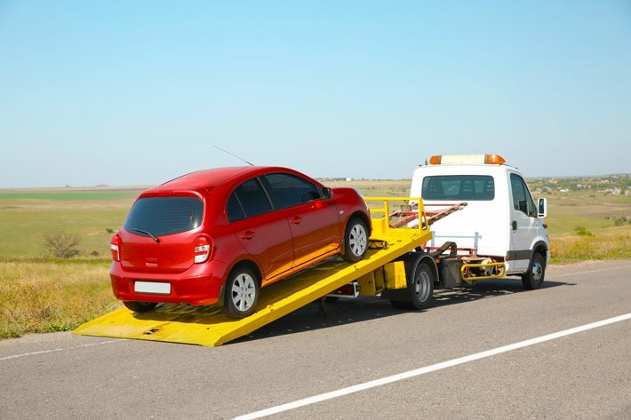 Une voiture rouge en panne est chargee sur une remorque depanneuse au bord de la route