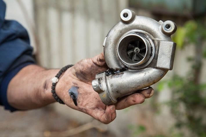 Une main couverte de cambouis tenant un turbo de voiture usagé