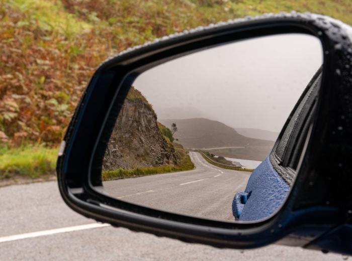 Rétroviseur extérieur de voiture bleu reflétant une route sinueuse en montagne