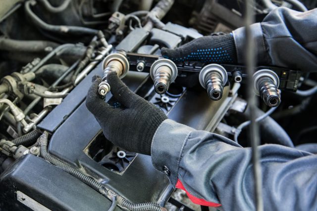 Mécanicien installant une bougie d'allumage neuve sur une rampe de bobines d'un moteur