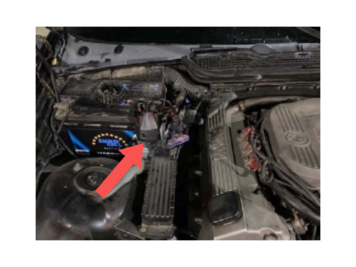 Vue sous le capot d'une BMW Série 3 E36 Phase 1 montrant la batterie avec une flèche rouge