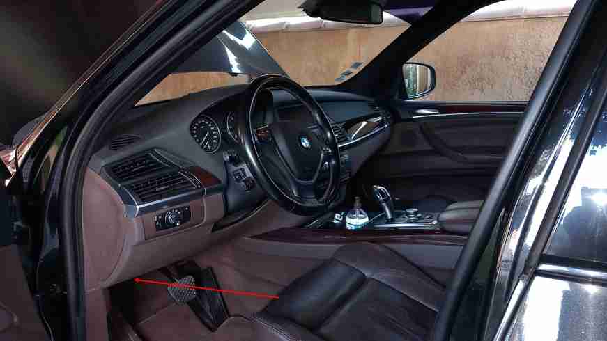 Une flèche rouge indique l'emplacement de la prise OBD dans l'habitacle d'une BMW X5 E70