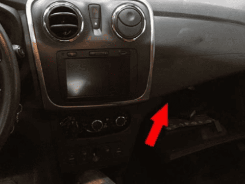 Une flèche rouge indique l'emplacement de la prise OBD2 sur le tableau de bord d'une Dacia Logan