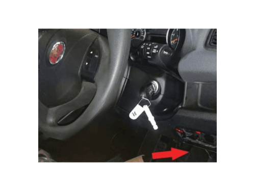Une flèche rouge indique l'emplacement de la prise OBD de diagnostic sur un tableau de bord de Fiat Doblo 2