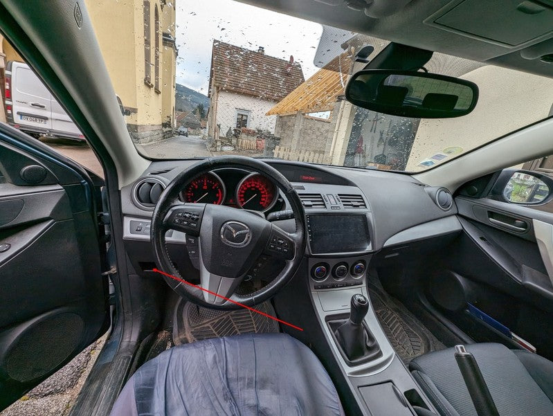 Vue de l habitacle d une Mazda 3 indiquant l emplacement de la prise de diagnostic OBD