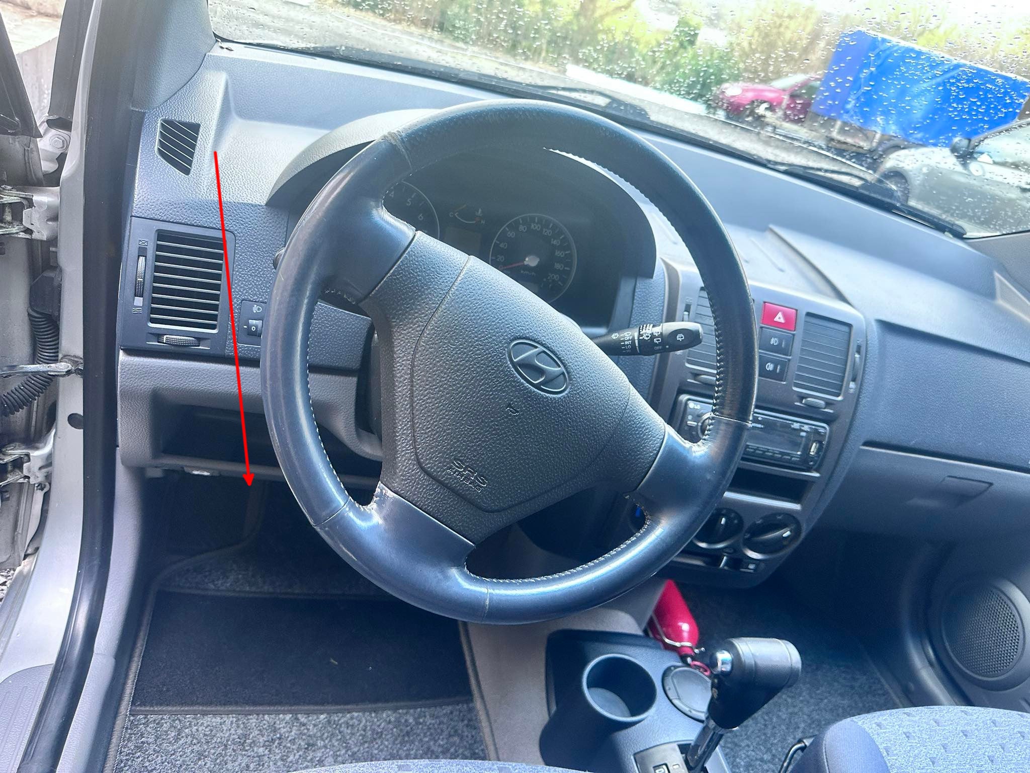 Une flèche rouge indique l'emplacement de la prise OBD pour valise de diagnostic sous le volant d'une Hyundai Getz