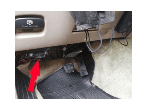 Une flèche rouge indique l'emplacement de la prise OBD2 sous le tableau de bord d'une Chevrolet Astro