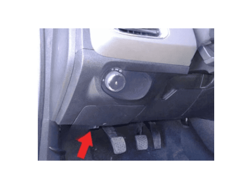 Une flèche rouge indique l'emplacement de la prise OBD2 sous le pédalier d'une Chevrolet Prisma 2