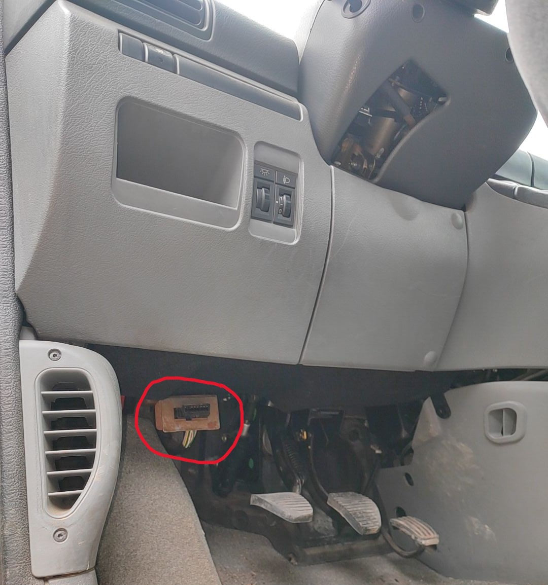 Prise de diagnostic OBD2 entouree en rouge sous le tableau de bord d une voiture