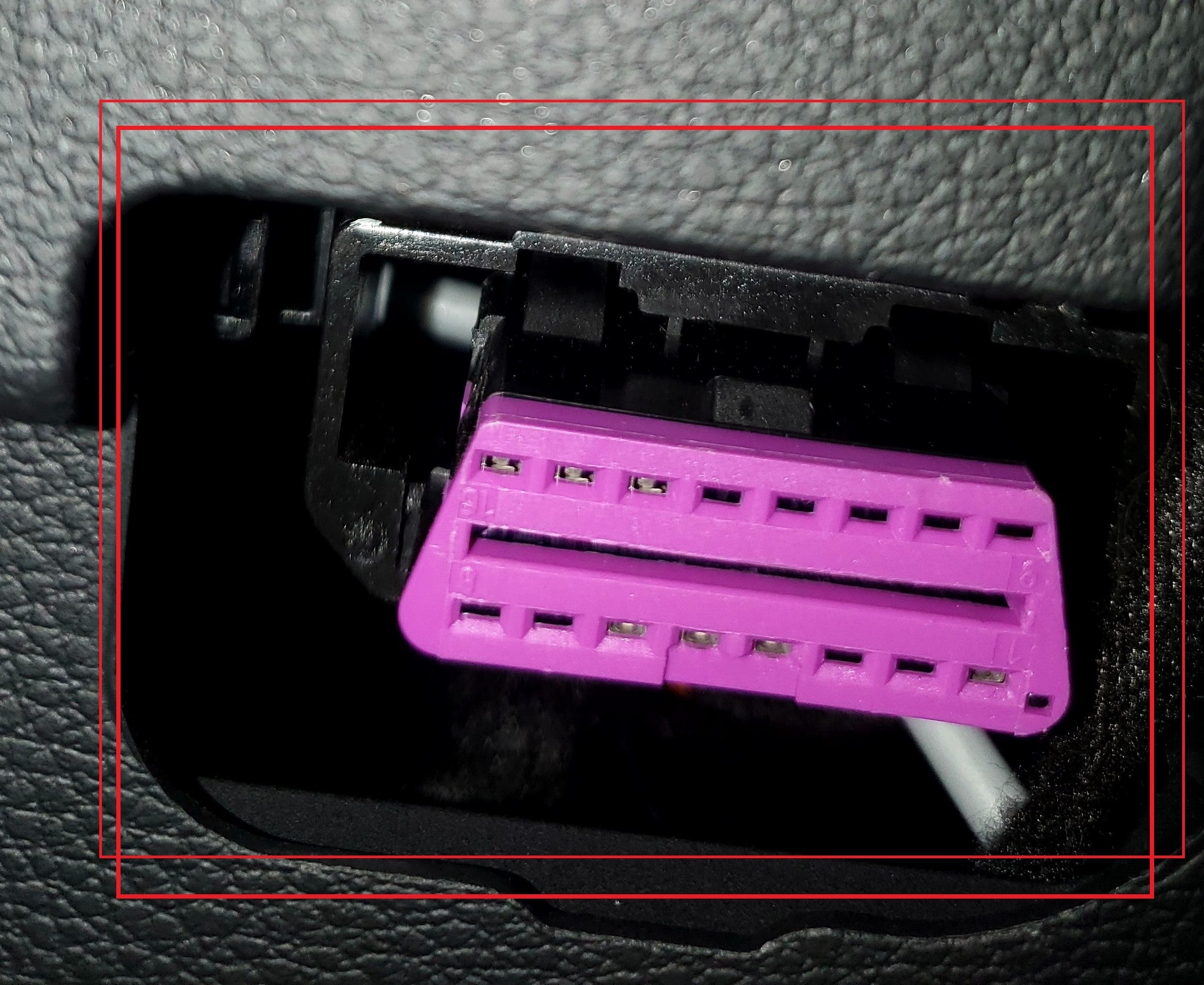 Gros plan sur la prise de diagnostic OBD2 violette sous le tableau de bord d'un véhicule
