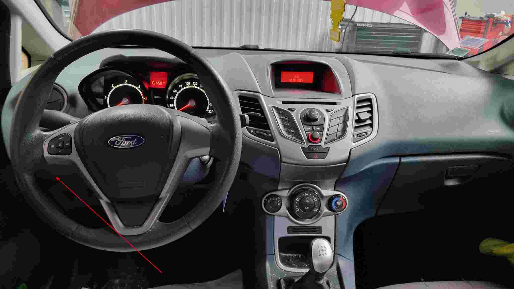 Vue intérieure de l'habitacle d'une Ford Fiesta avec flèche rouge indiquant la prise de diagnostic OBD2