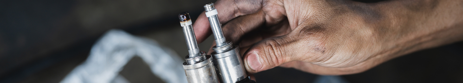 Comparaison de deux injecteurs de voiture tenus par les mains sales d'un mécanicien