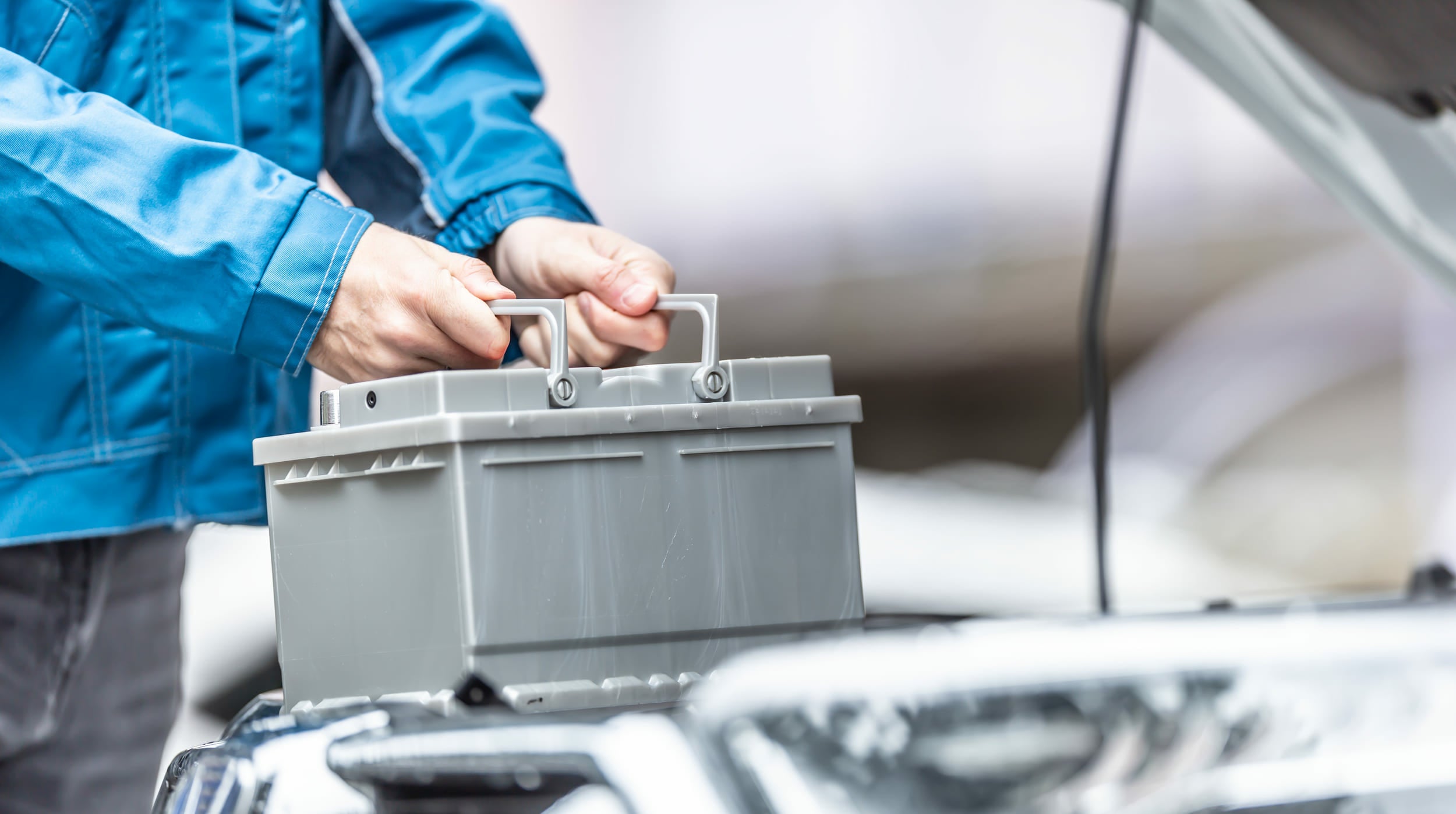 Meccanicien en veste bleue retirant une batterie de voiture usagée sous le capot