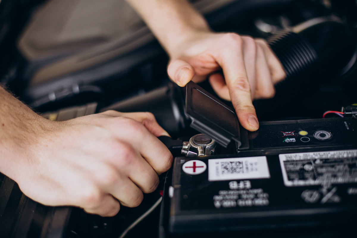 Mains d un technicien ouvrant le cache de protection d une batterie de voiture pour un test